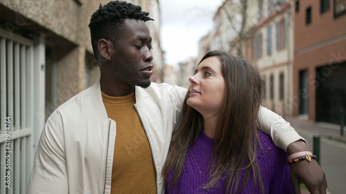 Interracial young couple walking together in city street. Black man arm around girlfriend