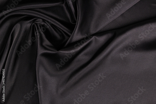 Beautiful elegant black background with drapery and wavy folds of silk satin material texture. Top view