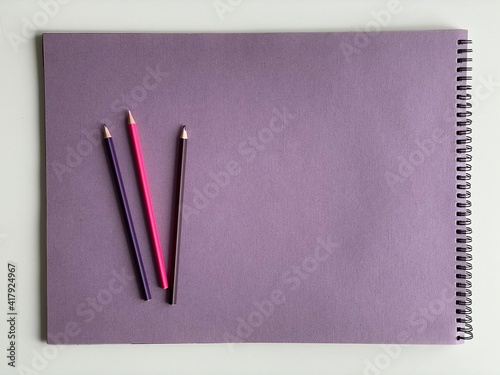 Colored pencils on purple paper album on white table. Artist, art and hobby. Drawing and painting