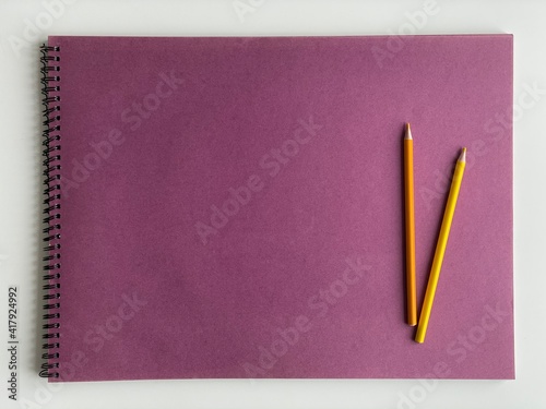 Colored pencils on purple paper album on white table. Artist, art and hobby. Drawing and painting