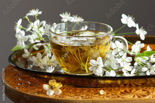 Cherry blossom tea in a glass cup with blooming floral branches nearby, healthy herbal drink is good for skin and heart, rich of antioxidants and essential acids, closeup, naturopathy concept