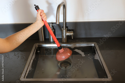 Overflowing kitchen sink, clogged drain. Hand holding plunger (force cup). Plumbing problems. photo