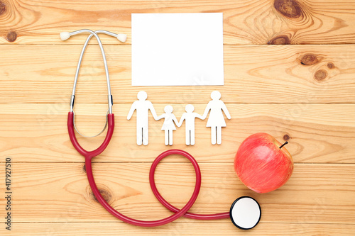 Text Doctor's Day with stethoscope, red apple and family figure on brown wooden table