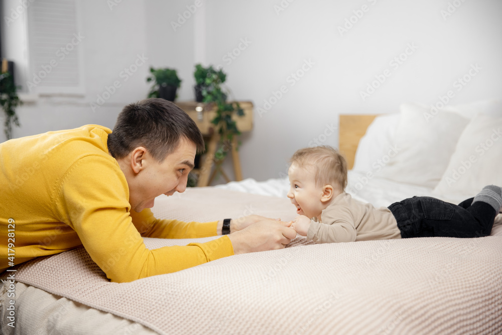 Young father is playing with newborn baby on bed