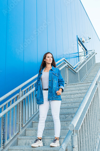 Lifestyle portrait of a beautiful and happy young woman walking down stairs in the street with blue background © Ana BG