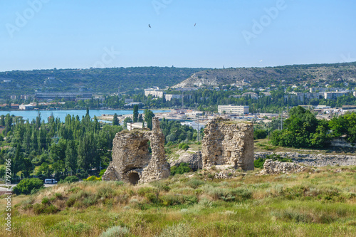 Panorama of medieval towers of Kalamita, fortress founded by Byzantines. It was built above cliff hiding cave church of St Clement. Modern city Inkerman (Crimea) and Sevastopol bay are on background photo