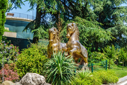 Old golden statues of rearing horses in city park Paradise  or Aivazovsky   Partenit  Crimea. Trees   exotic plants are around