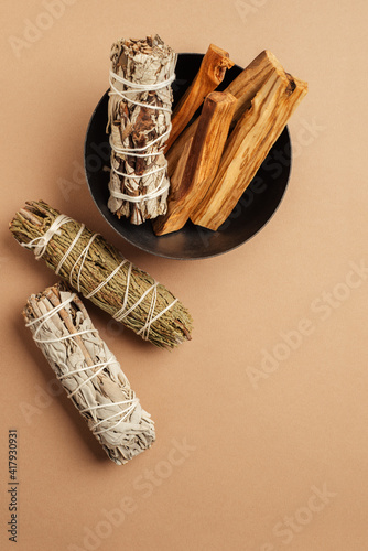 Set of incense for fumigation. White sage, cedar, yerba santa, and Palo Santo sticks tied in bunch in metal bowl. View from above. Organic holy tree incense from Latin America. Close-up color photo.