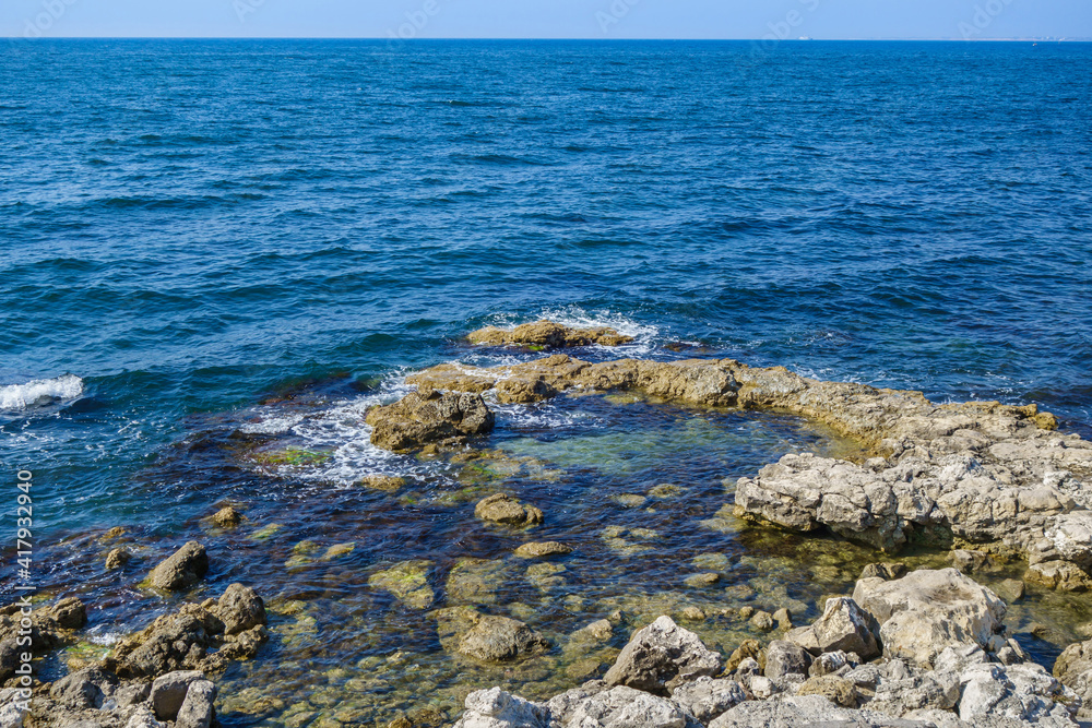Sea waves washing shore stones. Calm water, clear sky and small silhouette of ship on far horizon Sea waves washing shore stones. Calm water, clear sky and small silhouette of ship on far horizon