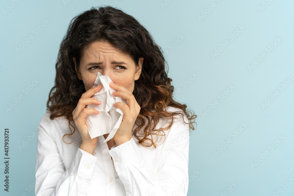 Studio portrait of young office employee woman in white blouse with tissue blowing nose, isolated on blue background, copy space. Rhinitis, seasonal allergy, symptoms of flu virus concept. Studio portrait of young office employee woman in white blouse with tissue blowing nose, isolated on blue background, copy space. Rhinitis, seasonal allergy, symptoms of flu virus concept.
