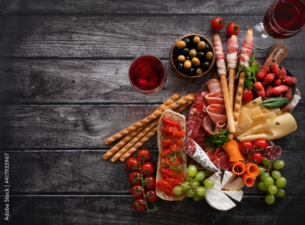 Antipasti, a traditional Italian appetizer and red wine on a dark wooden table. Sliced meat. Top view. Copy the space.