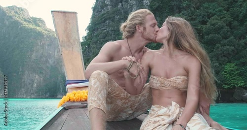 Romantic sweet couple sitting on the front of long tail boat seeing an amazing beautiful seascape of Phi Phi Islands and kiss each other with love during summer vacation travel in Phuket, Thailand.