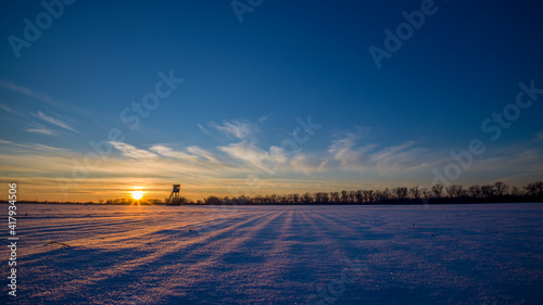 ein schneebedektes Feld mit einem Hochsitz mit untergehender Abendsonne