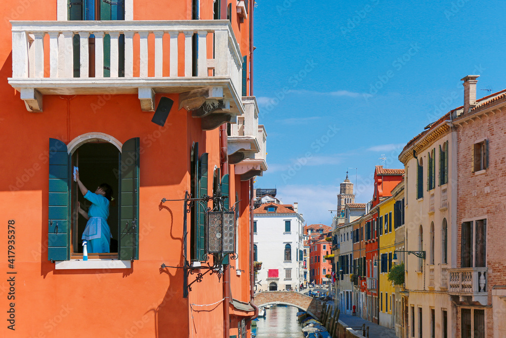 Woman cleaning window shades in colorful venice italy on sunny summer day with canals on side
