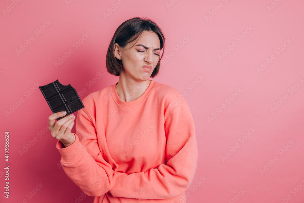 Naklejka premium Beautiful sad woman with abdominal pain with chocolate bar on pink background and bright makeup
