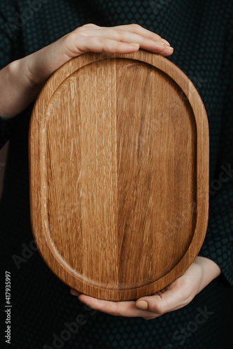 Woman holding an oval shaped wooden plate. Beautiful crockery made of real wood.