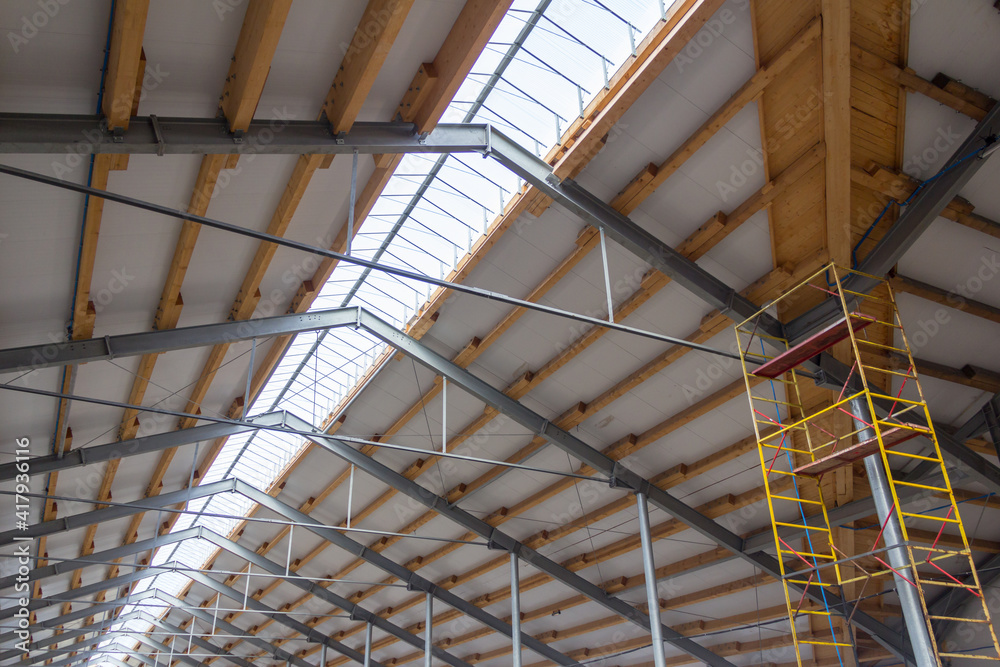 Obraz premium The roof structure of a large hangar consists of a steel frame and timber floor joists. Construction phase of a large complex on a farm
