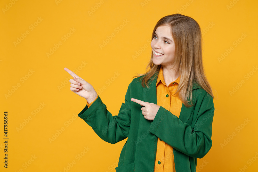 Little blonde kid girl 12-13 years old in casual clothes green shirt point index finger aside on copy space mock up isolated on yellow orange background children studio. Childhood lifestyle concept Little blonde kid girl 12-13 years old in casual clothes green shirt point index finger aside on copy space mock up isolated on yellow orange background children studio. Childhood lifestyle concept