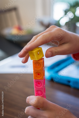 фотографія Child stacks yellow math counting cube during an e-learning activity; hybrid spe