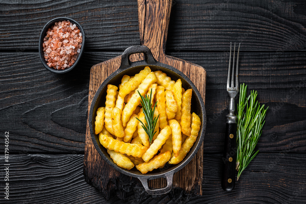 Fried Crinkle French fries potatoes in a pan. Black Wooden background. Top view