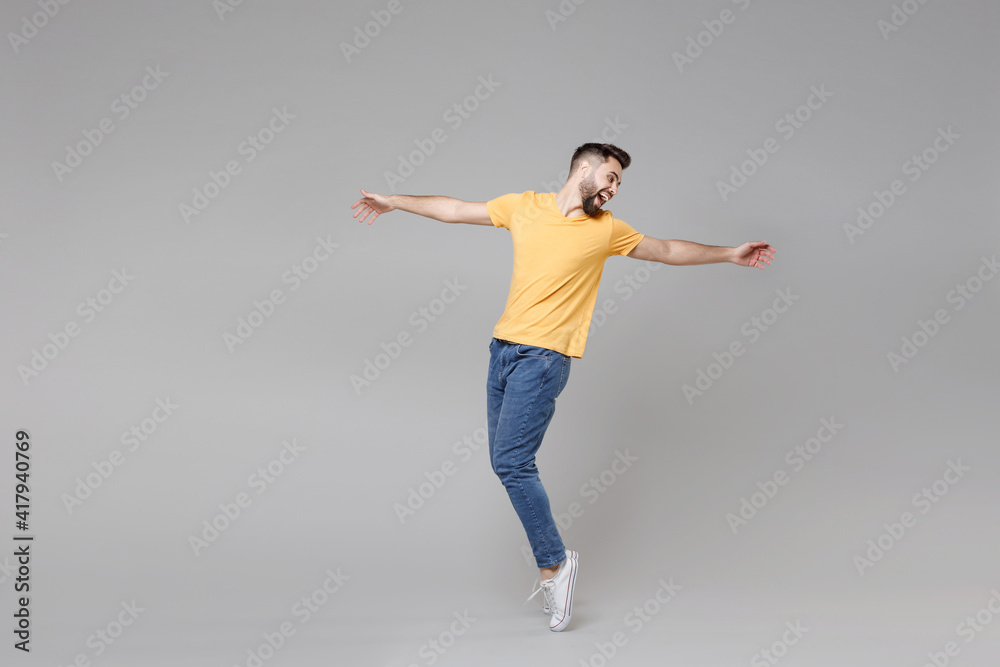 Fototapeta premium Full length of young bearded attractive handsome relaxed man 20s in casual yellow basic t-shirt with outstretched hand leaning over looking aside isolated on grey color background studio portrait.