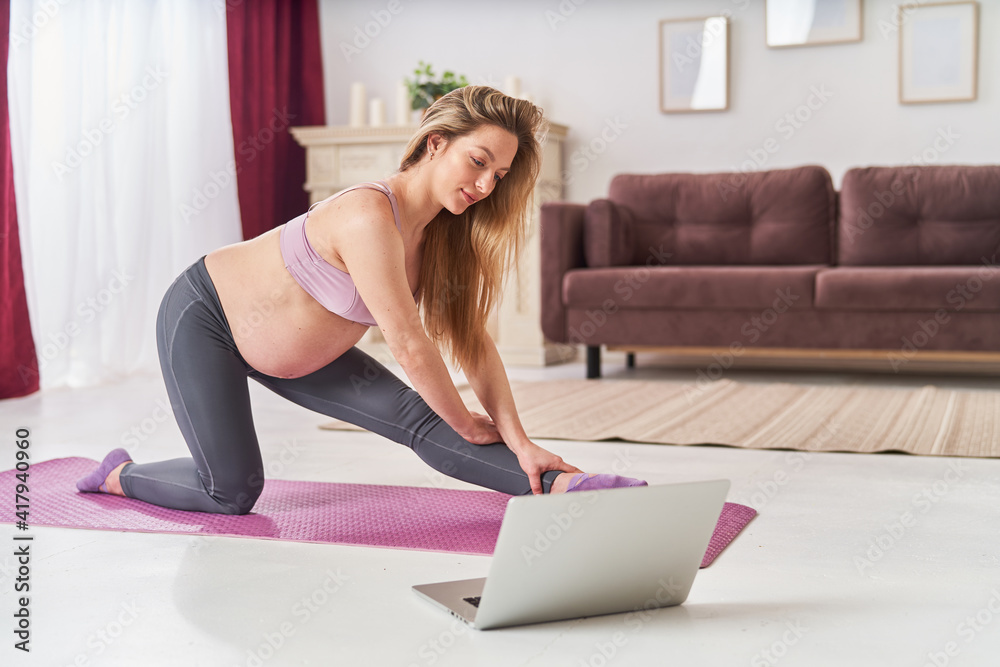Happy attractive pregnant woman in sports clothes, doing exercises on the gym mat at home in the living room. health during pregnancy. yoga classes at home. Motherhood, active pregnancy. Happy attractive pregnant woman in sports clothes, doing exercises on the gym mat at home in the living room. health during pregnancy. yoga classes at home. Motherhood, active pregnancy.