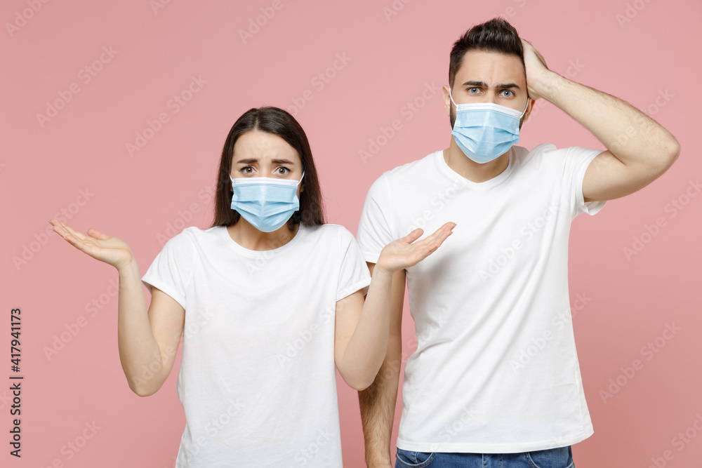 Young couple two friends man woman in white blank print design tshirts sterile face mask to safe from coronavirus virus covid19 on quarantine posing isolated on pastel pink background studio portrait