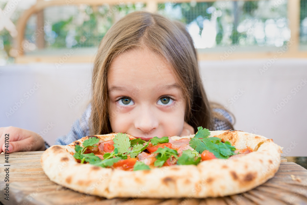 Hungry kid girl 5-6 years eating pizza on cafe terrace on sunny day. Family having fun outside the restaurant Hungry kid girl 5-6 years eating pizza on cafe terrace on sunny day. Family having fun outside the restaurant
