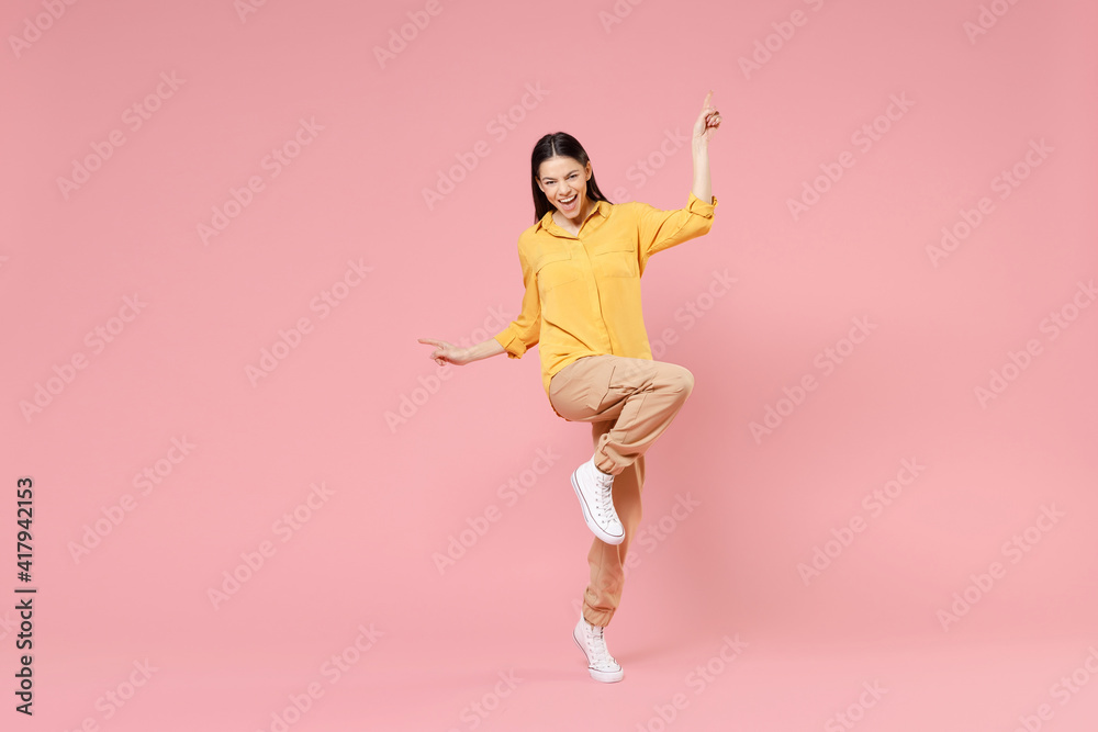 Full length of young brunette excited overjoyed attractive latin woman 20s in yellow casual shirt do winner gesture outstretched hands celebrating isolated on pastel pink background studio portrait.