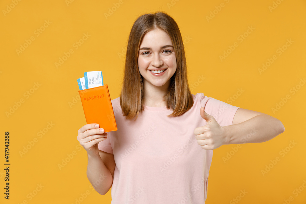 Traveler tourist woman in pastel pink t-shirt hold passport, tickets show thumb up like gesture isolated on yellow background. Passenger travel abroad, weekends getaway. Air flight journey concept. Traveler tourist woman in pastel pink t-shirt hold passport, tickets show thumb up like gesture isolated on yellow background. Passenger travel abroad, weekends getaway. Air flight journey concept.