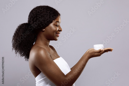 Attractive Black Female Wrapped In Towel After Bath Holding Jar With Cream