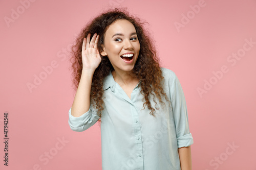 Quadro em tela Young black african happy smiling curly curious nosy woman 20s wearing casual blue shirt try to hear you overhear listening intently looking camera isolated on pastel pink background studio portrait