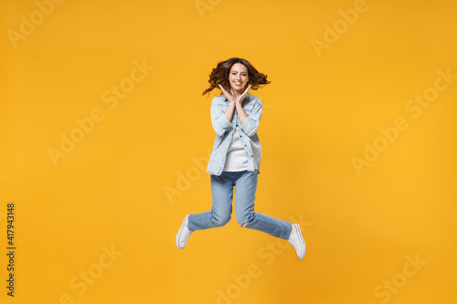 Full length of young overjoyed surprised excited shocked fun student happy woman 20s wearing denim shirt white t-shirt spread hands celebrating jump high isolated on yellow background studio portrait © ViDi Studio