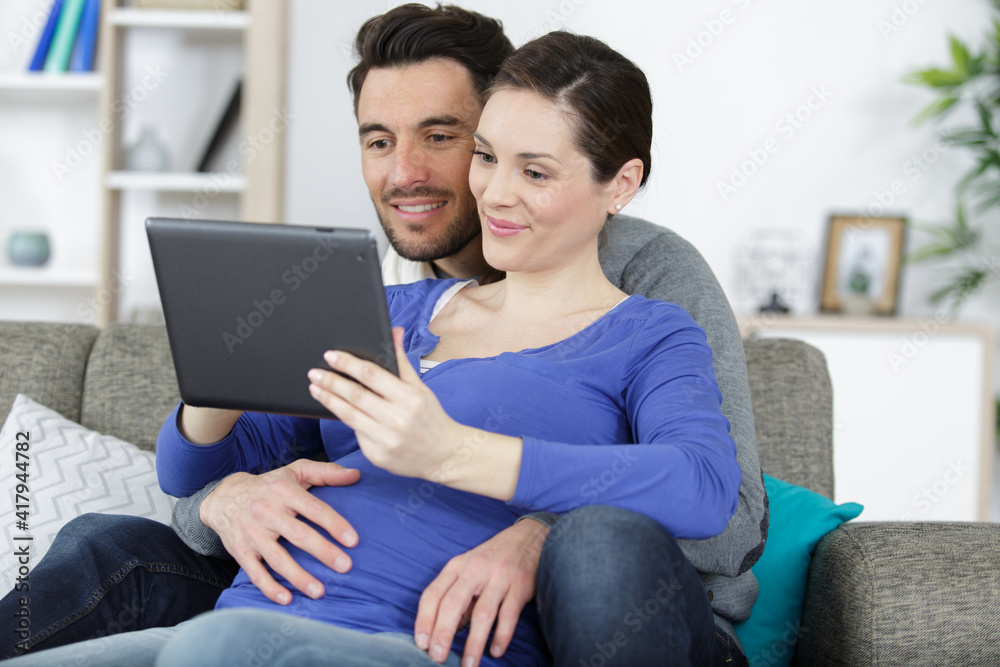 couple pregnant woman and husband looking tablet
