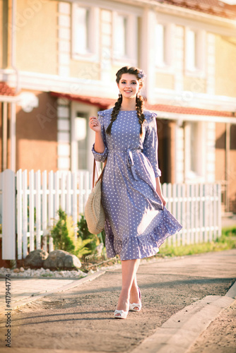 Beautiful young smiling woman in a blue dress walks down the street on a sunny day
