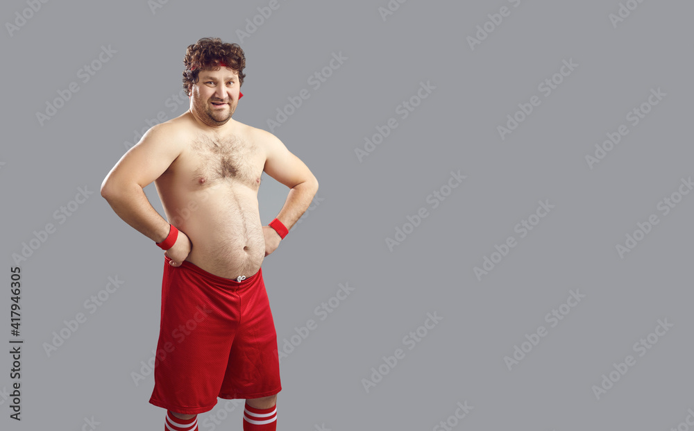 Portrait of funny fat man in sports shorts and leggings adjusts to sport  standing on gray