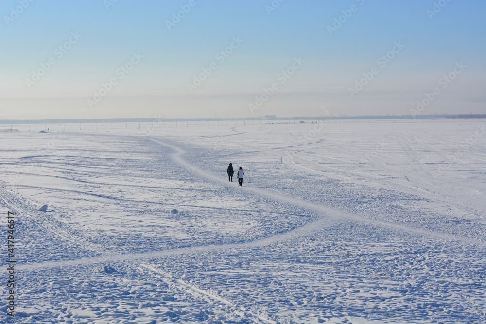 two people cross to the other side of the frozen river. sunny frosty day. winter continues.