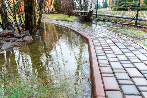 Принти на полотні Garden bushes, tree and green grass lawn covered with water due to snow melting thaw and flash high water at spring