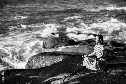 Yoga woman meditating on rocks ocean beach in calm weather. Black and white photo.
