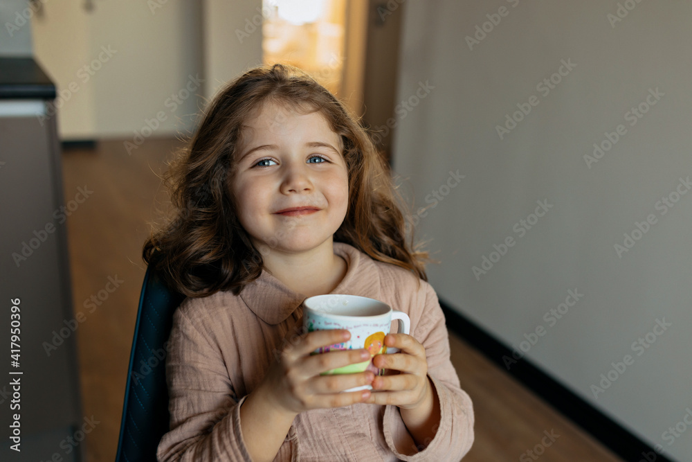 Close up portrait of charming pretty girl with wavy hair wearing pajamas drinking tea in the kitchen Close up portrait of charming pretty girl with wavy hair wearing pajamas drinking tea in the kitchen
