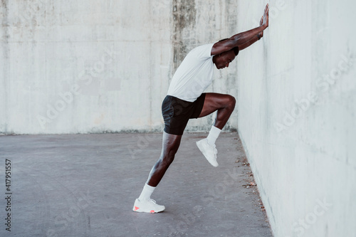 Sportsman doing stretching workout while leaning on white wall photo