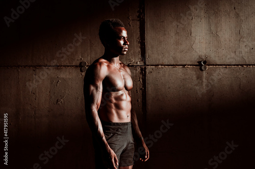 Sportsman with bare chested standing against gray wall during sunset