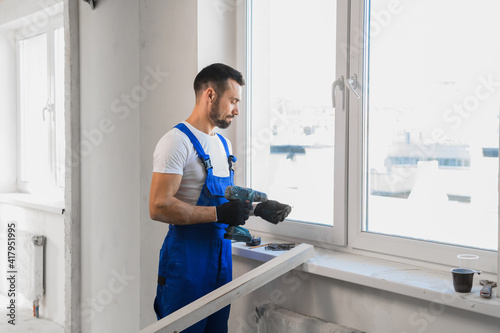 A man in blue work clothes stands against the wall and showing thumb