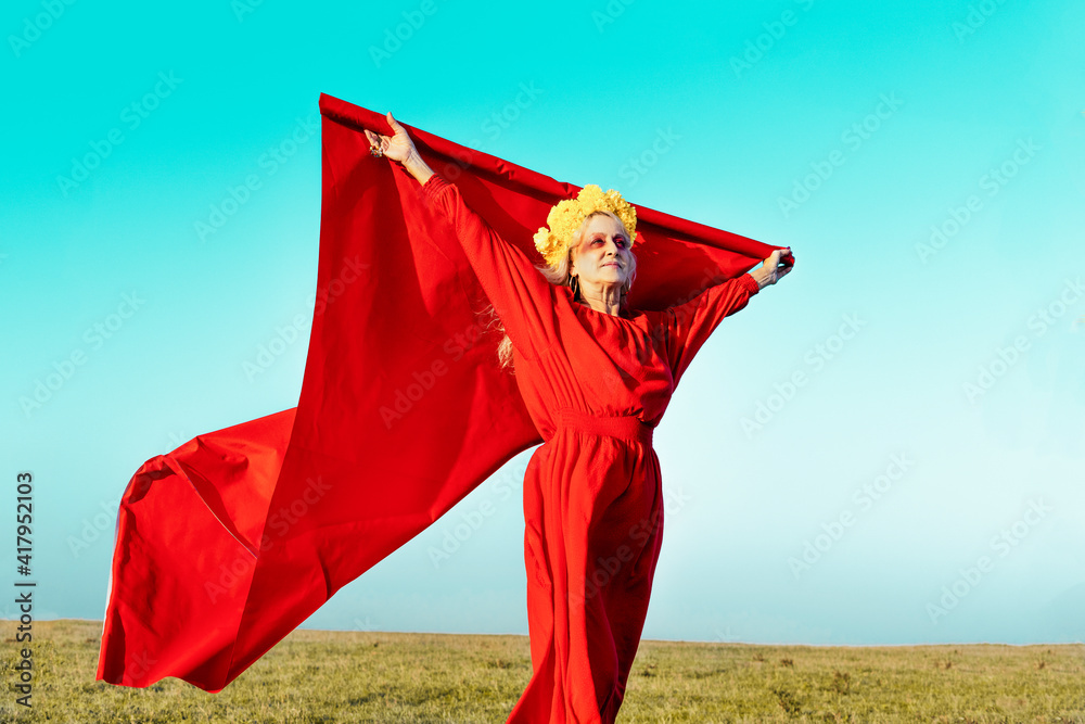 Woman holding red fabric while standing on grass against blue sky Woman holding red fabric while standing on grass against blue sky