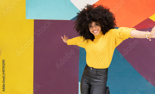 Carefree woman dancing with arms outstretched against multi colored wall photo