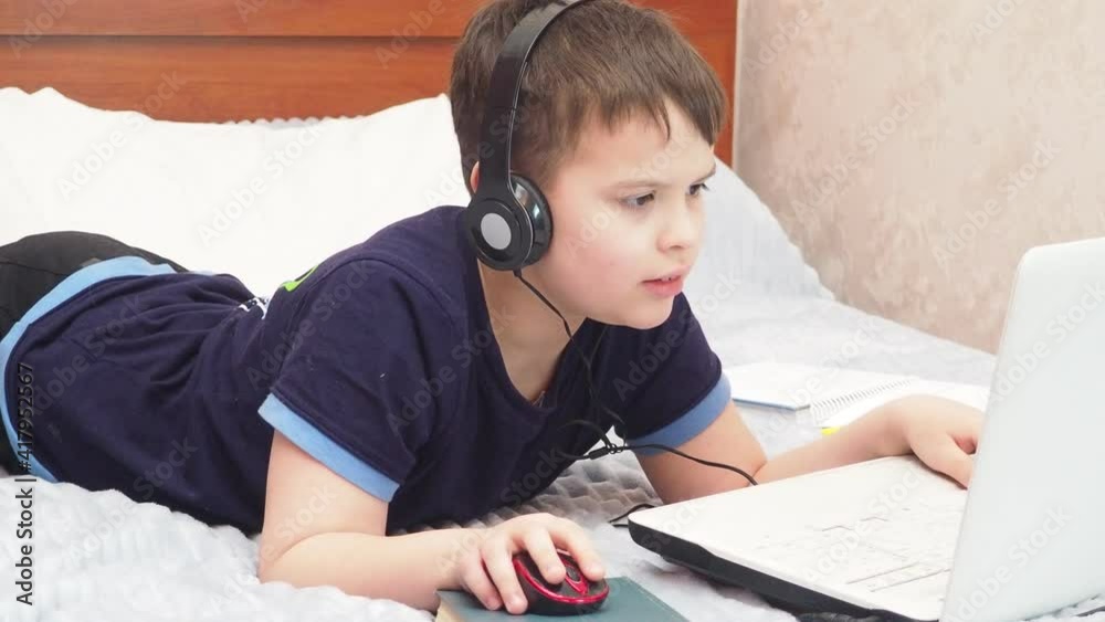 young boy playing in his computer or tablet and sitting in the bed. online games, stream or undergoes online training, online courses, studies at home during quarantine young boy playing in his computer or tablet and sitting in the bed. online games, stream or undergoes online training, online courses, studies at home during quarantine