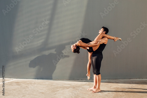 Young man helps flexible woman do dance pose against wall photo