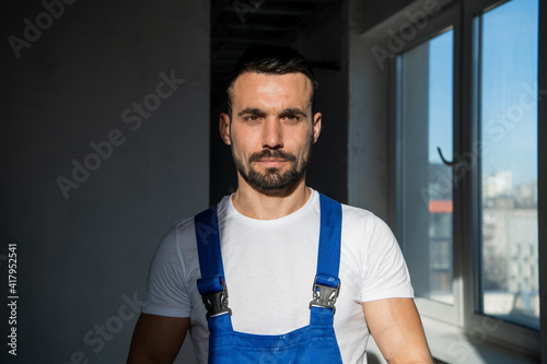 The handyman stands in a dark room. He is wearing blue work clothes