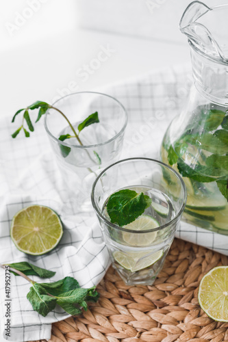 Detox water with lime fruit and mint leaves in jar and glasses