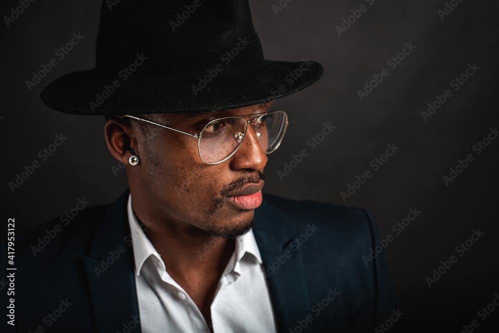 Portrait of attractive, handsome, pretty, serious and stylish professional african american businessman executive with stylish suit and white shirt and black hat isolated on dark background. Low key. Portrait of attractive, handsome, pretty, serious and stylish professional african american businessman executive with stylish suit and white shirt and black hat isolated on dark background. Low key.